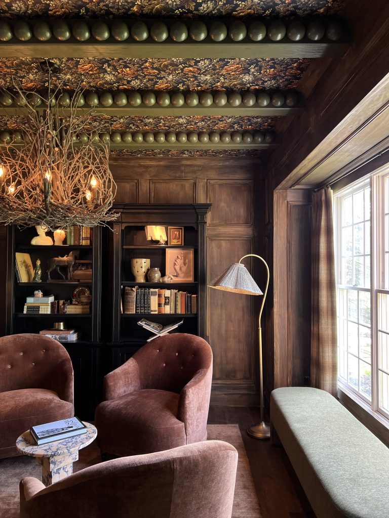 living room with painted green beams and bobbin trim and wood stained millwork on walls with black bookshelves