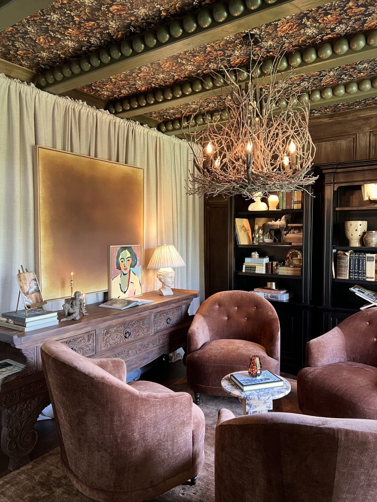living room with painted green beams and bobbin trim and wallpaper on the ceiling with fabric on the walls and a twig chandelier and modern art